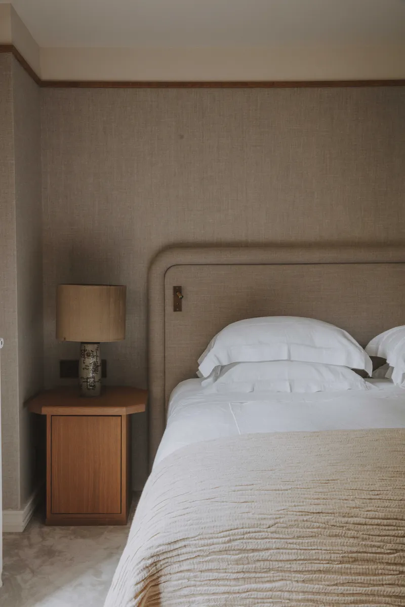 Tête de lit zen avec mur en tissu, moquette beige et table de chevet classique.