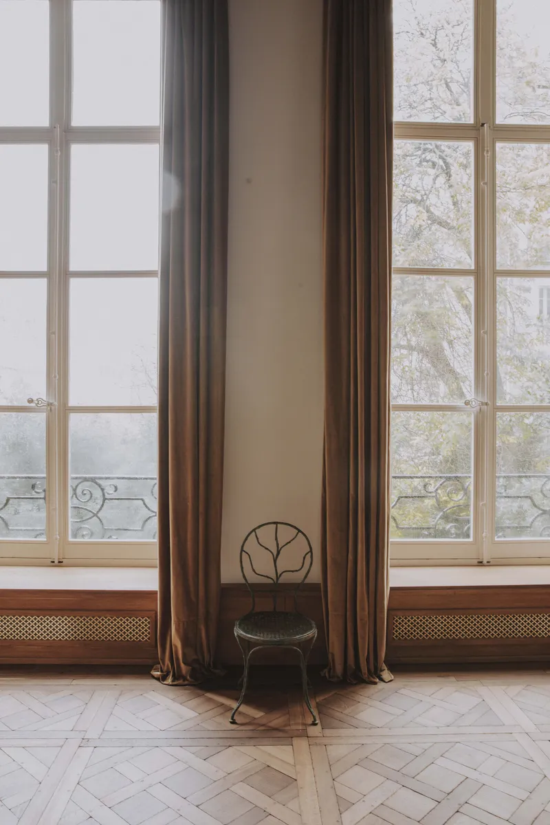Vue sur jardin avec chaises Giacometti et rideaux Nobilis dans un salon parisien.