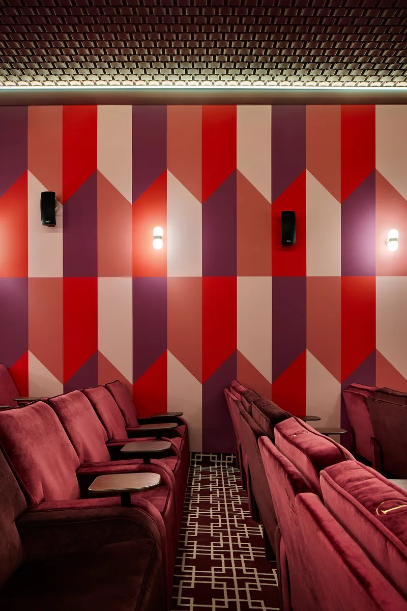 Tablet-arm cinema seats in Le Studio, with a chevron wall, opal sconces and geometric carpet.