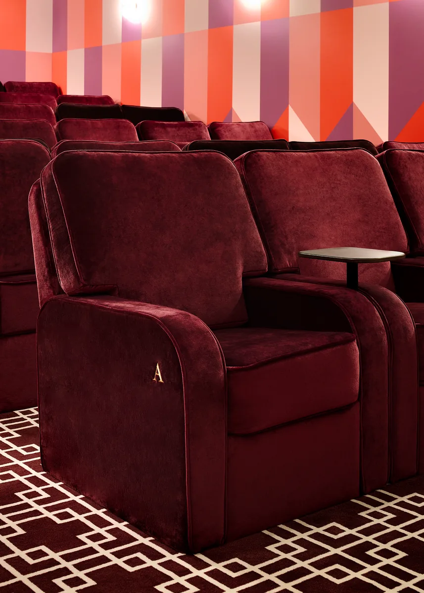Bespoke cinema seat in monogrammed raspberry velvet, swivel tablet, wide cushioned seat.