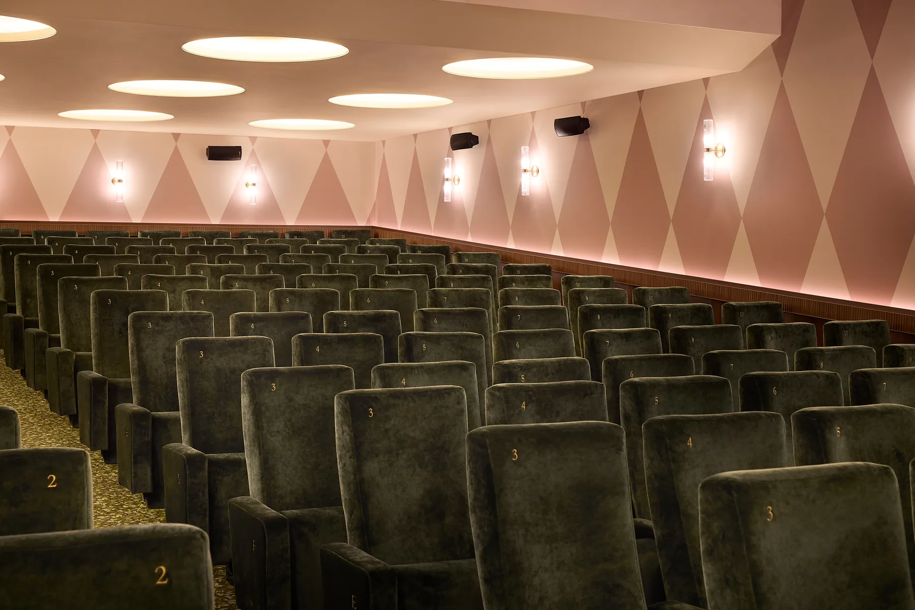 Wide view of an art-house auditorium, with deep tiers, round ceiling lights and gilded numbering.
