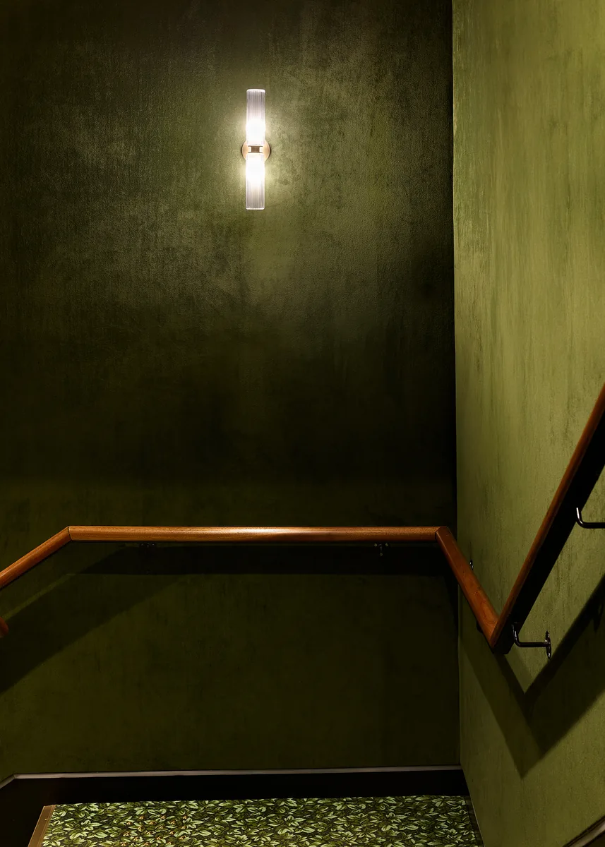 Cinema stair lined in green velvet, with a fluted sconce and timber handrail.