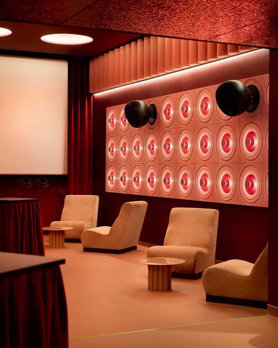 Lounge layout for cocktail screenings, with movable beige armchairs, side tables and a burgundy curtain.