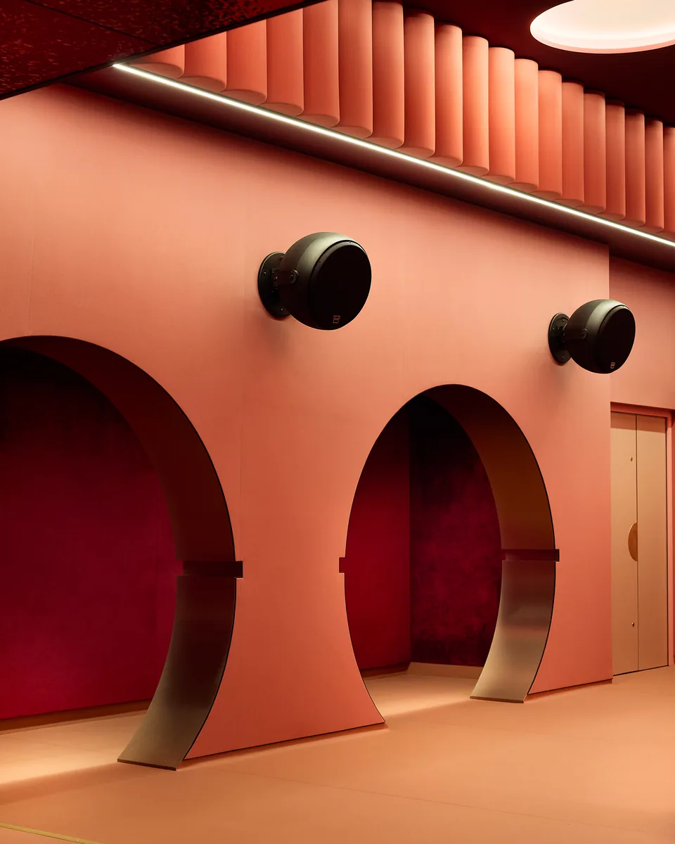Arched cinema circulation in salmon pink, with a fluted ceiling, round speakers and access to the rooms.
