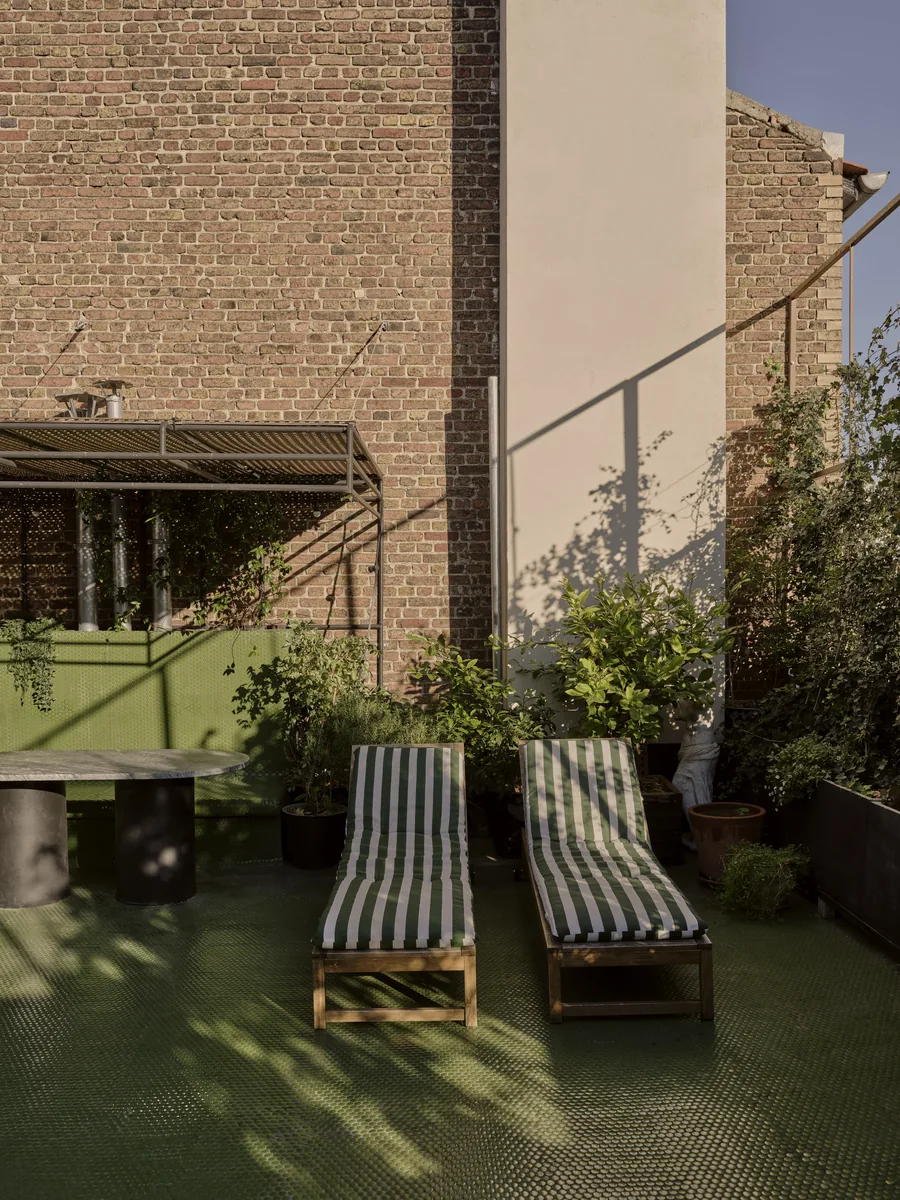Toit-terrasse avec bains de soleil rayés vert, pergola en métal et table ronde en marbre.
