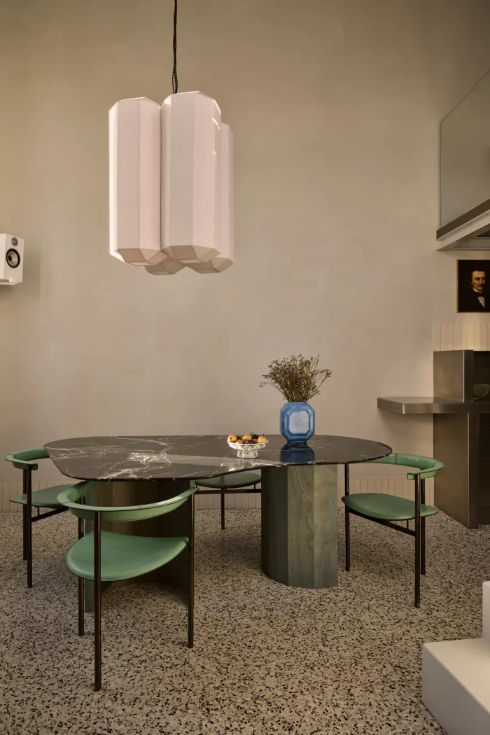 Salle à manger avec table en marbre dessinée sur mesure, suspension en lin, chaises en cuir vert et sol en terrazzo.
