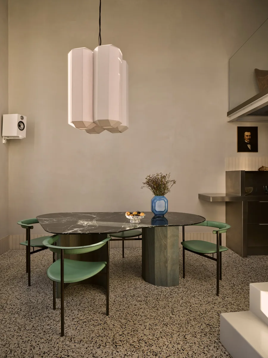 Salle à manger avec table en marbre dessinée sur mesure, suspension en lin, chaises en cuir vert et sol en terrazzo.