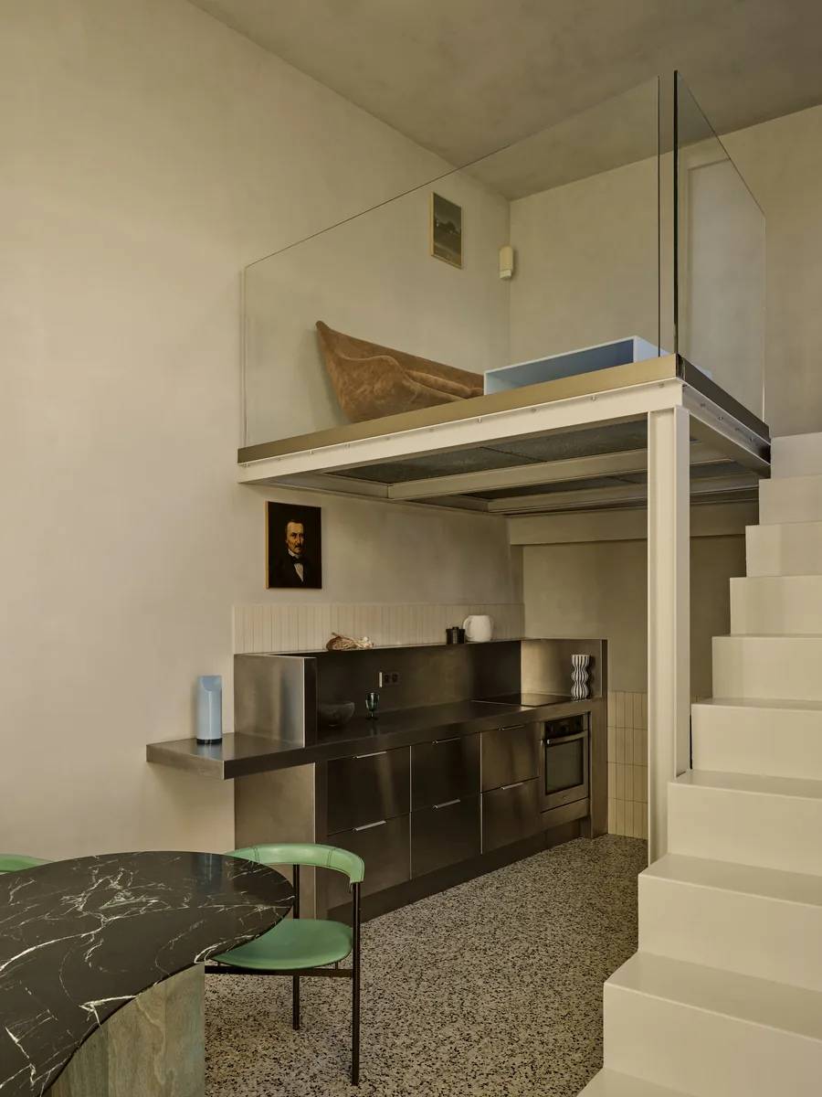 Cuisine en inox brossé sous la mezzanine, double volume, escalier en béton et portrait de famille.