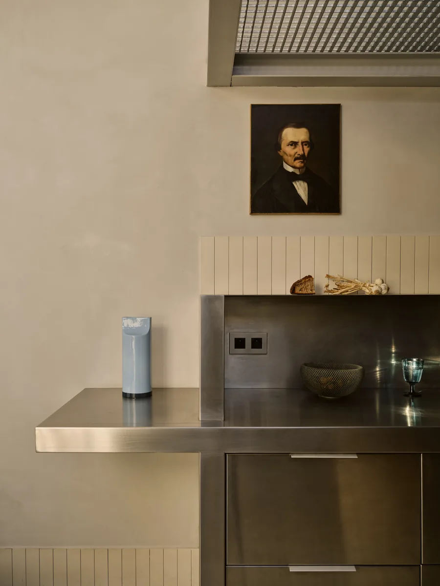 Détail de la cuisine en inox et carrelage cannelé, hotte inox et portrait de l'arrière-grand-père.