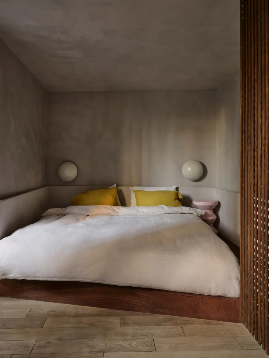 Chambre en alcôve avec lit plateforme en bois, claustra, appliques globe et linge de lin.