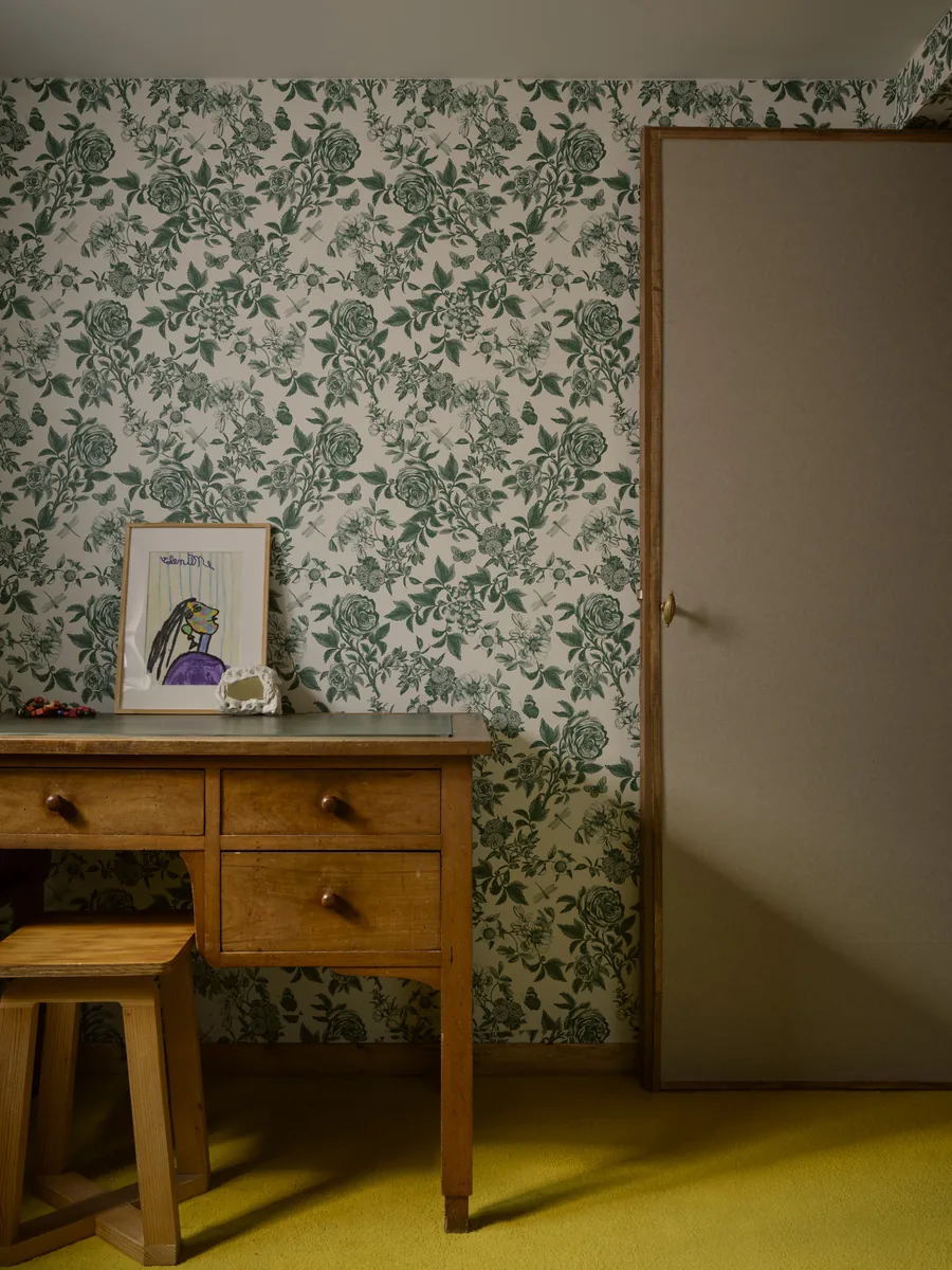 Chambre d'enfant avec bureau chiné, papier peint fleuri, moquette jaune et porte tendue de toile.